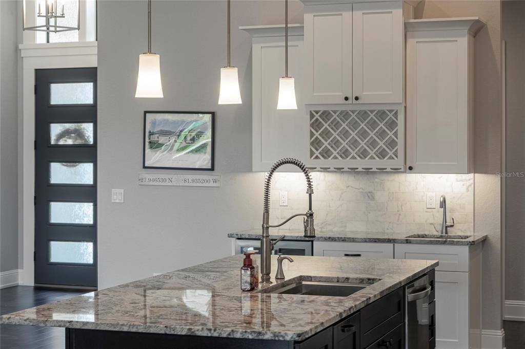 A kitchen island with granite countertops sits in front of white cabinets and a wet bar — 6545 EMERALD WOODS LANE, LAKELAND, FL