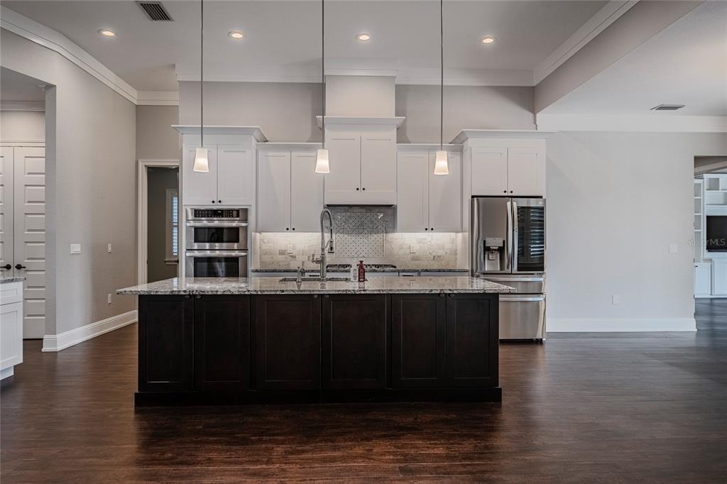 A kitchen features a dark wood island, white cabinetry, stainless steel appliances, and hardwood floors — 6545 EMERALD WOODS LANE, LAKELAND, FL