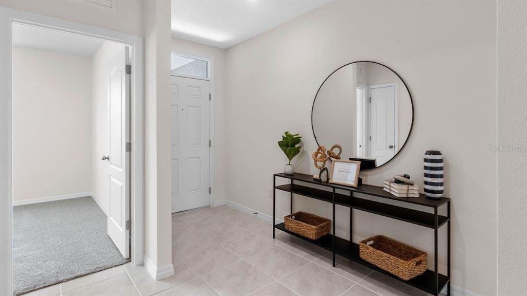 A bright entryway features tile flooring, a console table with decor, and a round mirror — 3740 GIORGIO DRIVE, WINTER HAVEN, FL