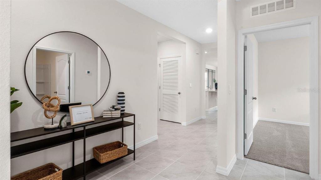 A hallway with light tile flooring features a black console table, a round mirror, and doorways — 3740 GIORGIO DRIVE, WINTER HAVEN, FL