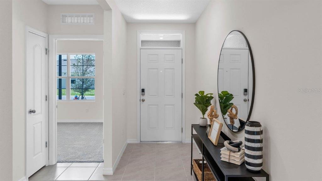 A bright entryway features a white front door, a console table, and an oval mirror — 3740 GIORGIO DRIVE, WINTER HAVEN, FL