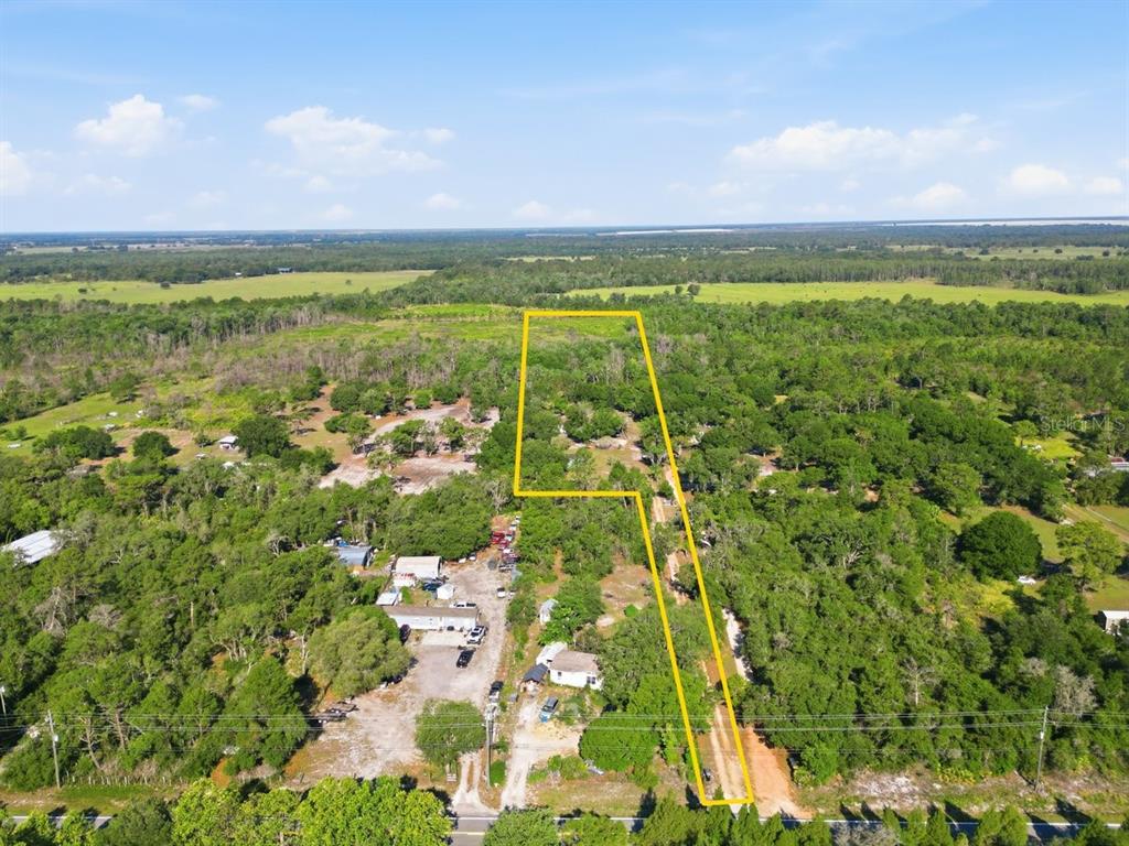 An aerial view shows a wooded lot outlined in yellow near a rural road — 1560 MCCLELLAN ROAD, FROSTPROOF, FL