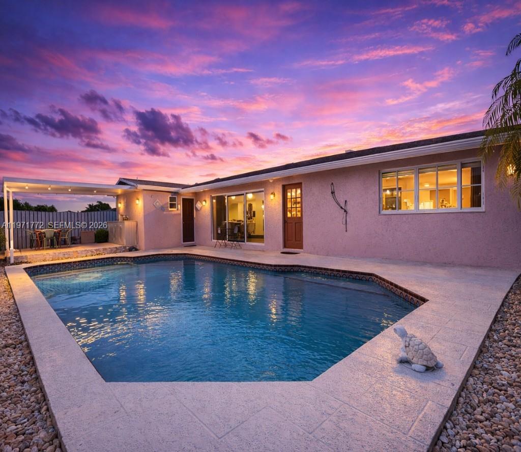 A backyard swimming pool sits in front of a house with a pink exterior — 11827 NW 39th St, Sunrise FL 33323, SUNRISE, FL