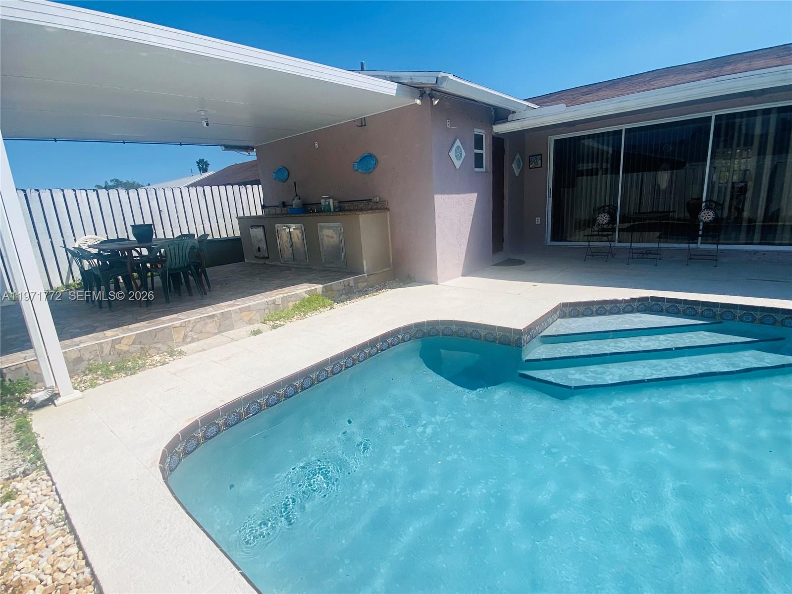 A backyard features a swimming pool, a covered patio with an outdoor kitchen, and seating — 11827 NW 39th St, Sunrise FL 33323, SUNRISE, FL