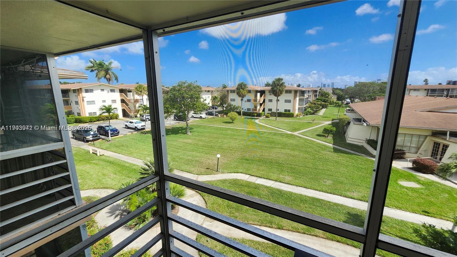 A view from a screened balcony overlooks a grassy courtyard between apartment buildings — 16901 NE 13th Ave # 306, Miami FL 33162, MIAMI, FL