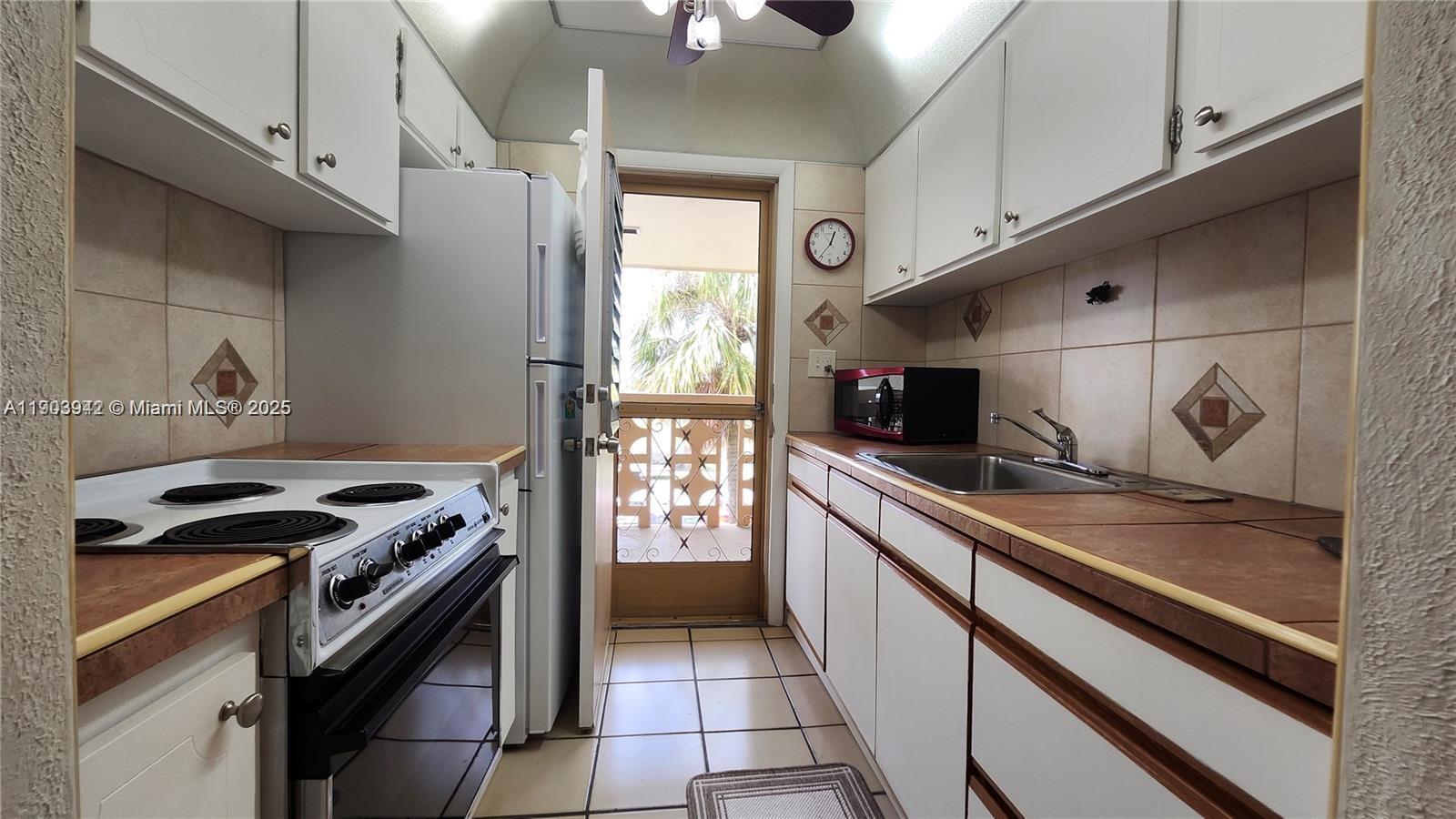 A galley kitchen features white cabinets, tiled countertops, a stove, and a door to a balcony — 16901 NE 13th Ave # 306, Miami FL 33162, MIAMI, FL