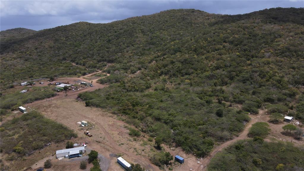 An aerial view shows a rural landscape with a hillside, dirt paths, and several structures — PR 250 KM 2.5 BO FLAMENCO Y SAN ISIDRO, CULEBRA, PR