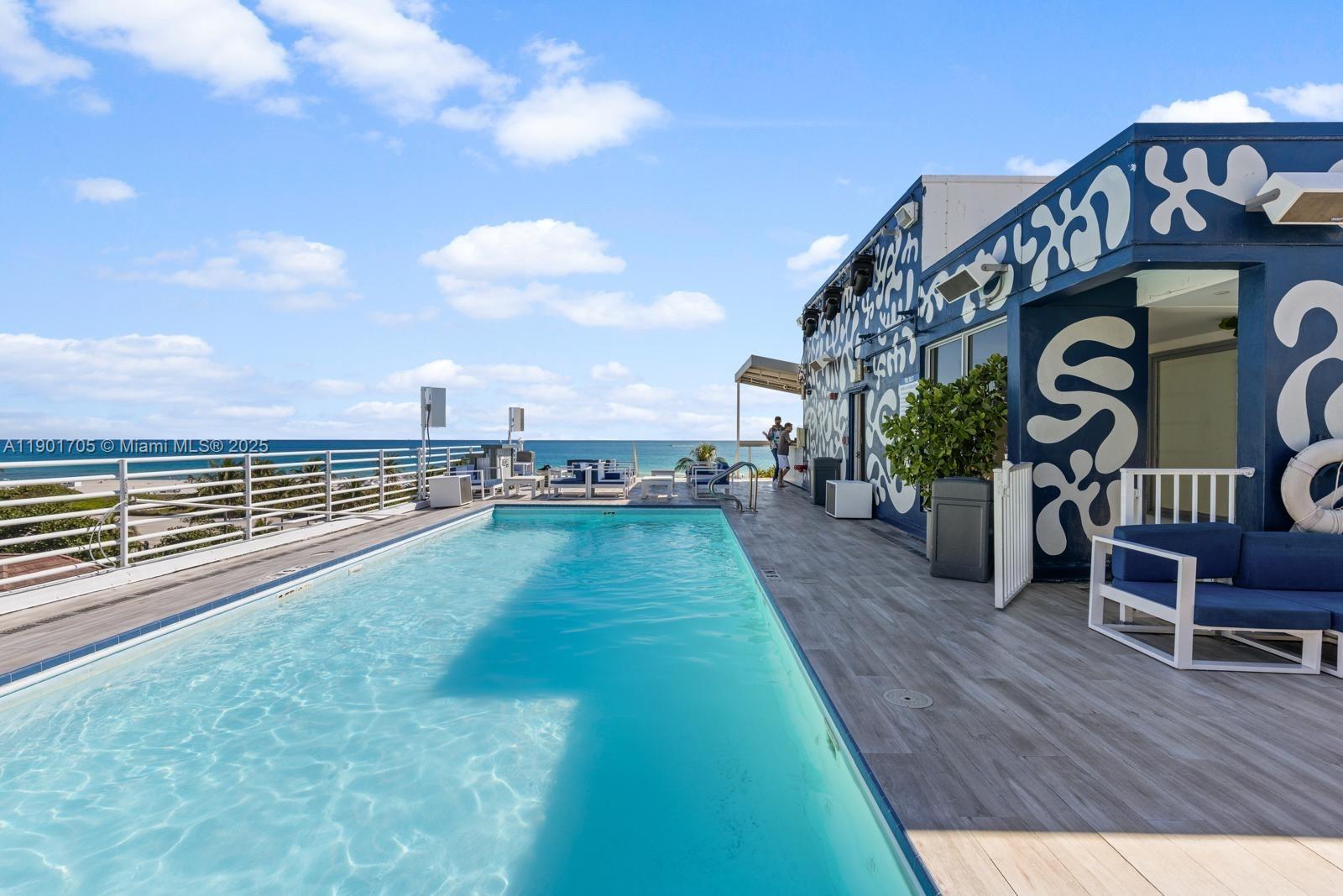 A rooftop swimming pool overlooks the ocean with a blue-and-white patterned building wall nearby — 1024 Ocean Dr # A301, Miami Beach FL 33139, MIAMI BEACH, FL