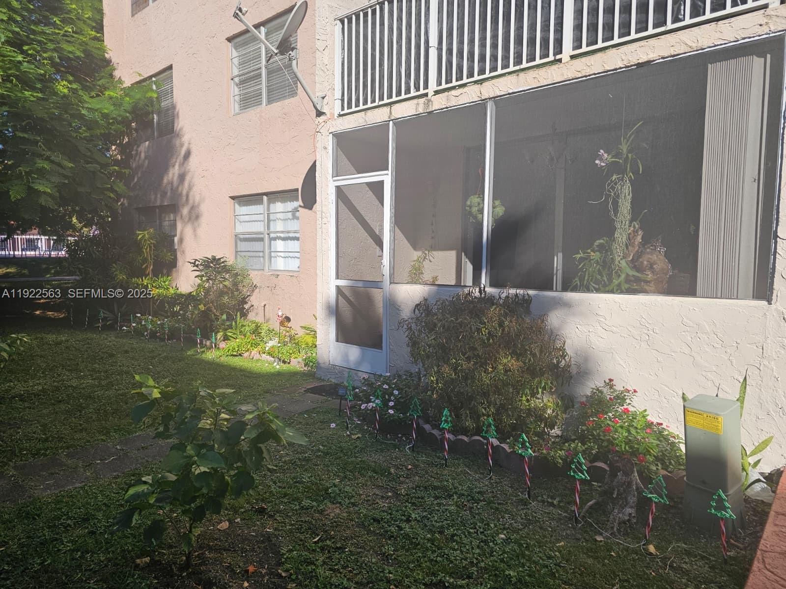 An exterior view of a ground-floor apartment with a screened-in patio and landscaped yard — 8411 NW 8th St # 111, Miami FL 33126, MIAMI, FL