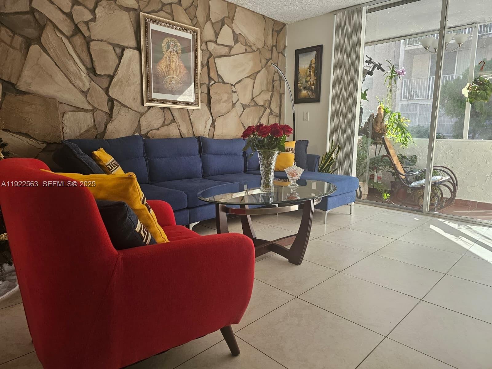 A living room features a blue sectional sofa, a red armchair, and a stone wall — 8411 NW 8th St # 111, Miami FL 33126, MIAMI, FL