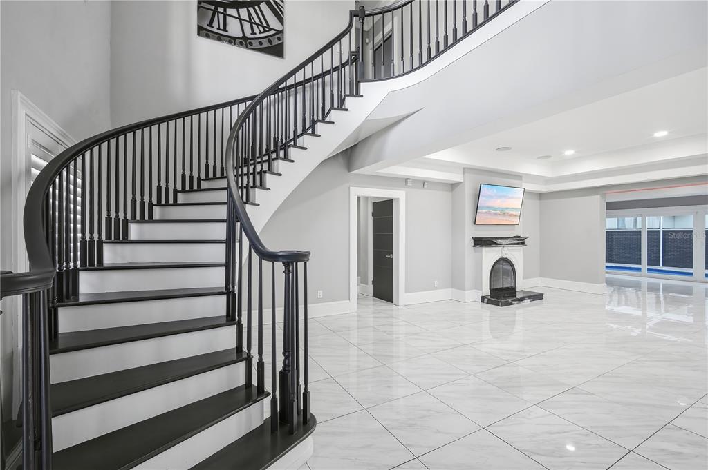 A curved staircase with black railings stands in a room with white marble-look tile flooring — 2418 W PALM DRIVE, TAMPA, FL