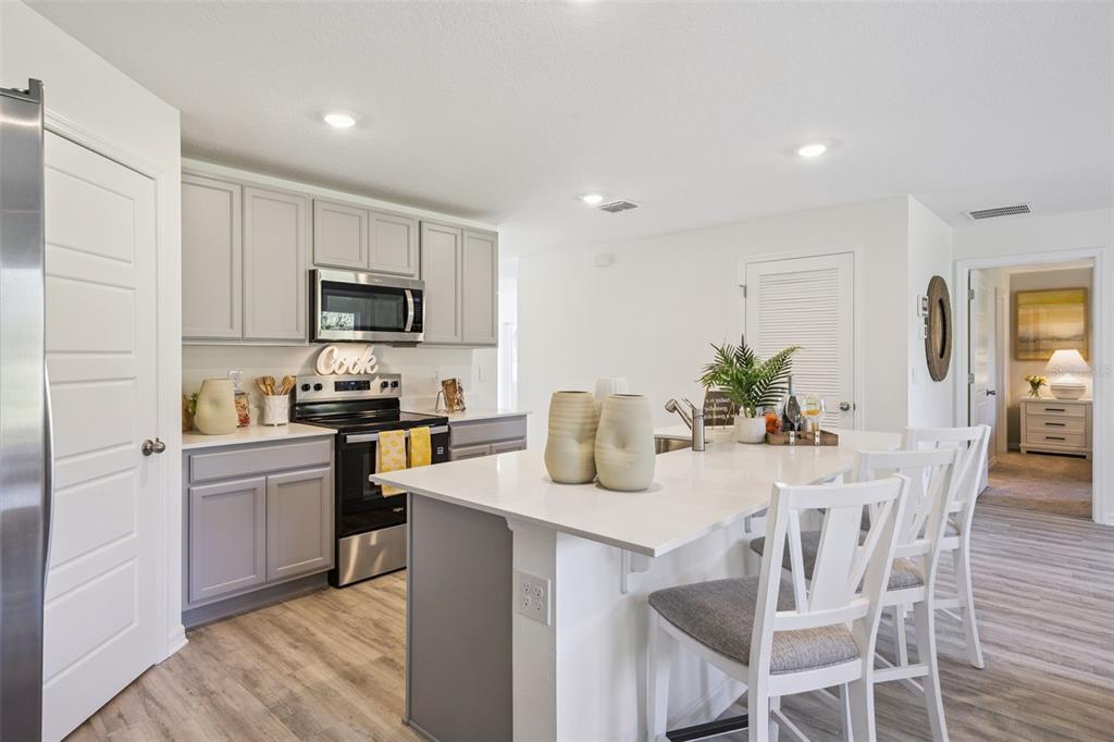 A kitchen features gray cabinets, white countertops, a center island, and light wood-look flooring — 1727 GRANDIOSE DRIVE, HAINES CITY, FL