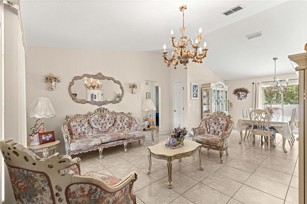 A formal living and dining room with tiled floors, ornate furniture, and two chandeliers — 4 CEDAR TRACE PASS, OCALA, FL