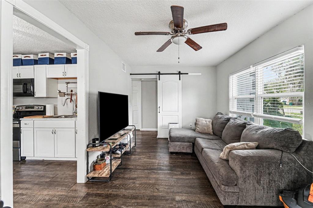A living room with dark wood floors, a gray sectional sofa, and a sliding barn door — 1024 GRANT AVENUE, MOUNT DORA, FL