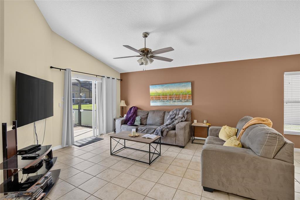 A living room features tile flooring, a vaulted ceiling, a brown accent wall, and furniture — 110 SARAGOSSA AVENUE, DAVENPORT, FL