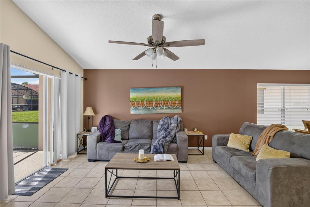 A living room features a vaulted ceiling, tile flooring, two gray sofas, and sliding doors — 110 SARAGOSSA AVENUE, DAVENPORT, FL