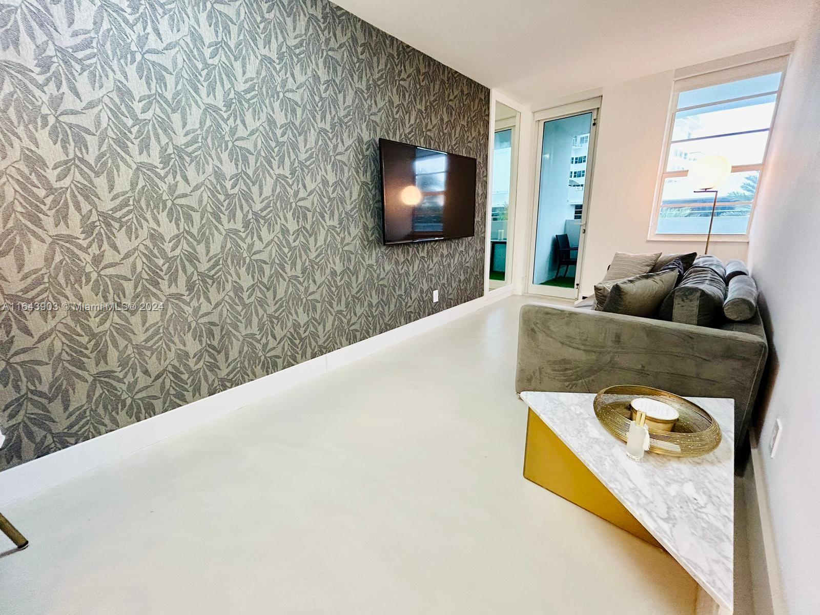 A living room features a patterned accent wall, a wall-mounted television, and a gray sofa — 100 Lincoln Rd # 445, Miami Beach FL 33139, MIAMI BEACH, FL