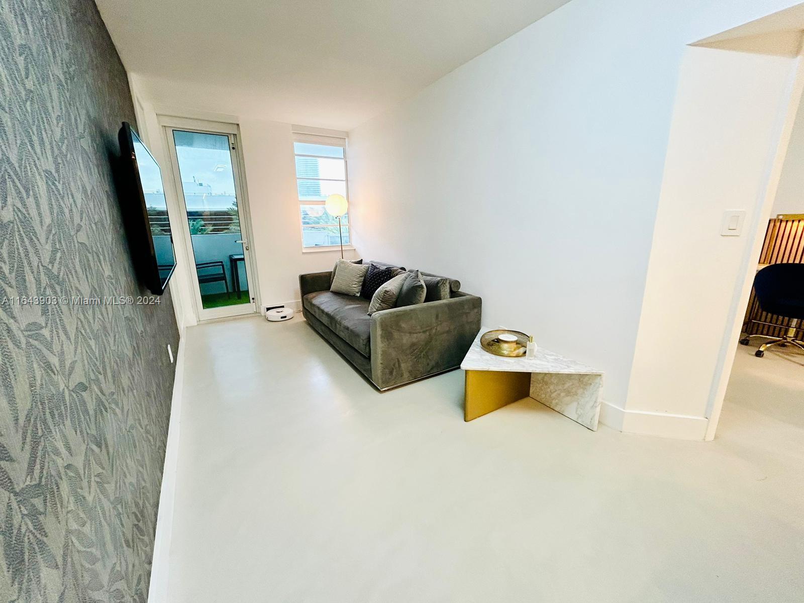 A living room features a grey sofa, a triangular marble table, and a patterned accent wall — 100 Lincoln Rd # 445, Miami Beach FL 33139, MIAMI BEACH, FL