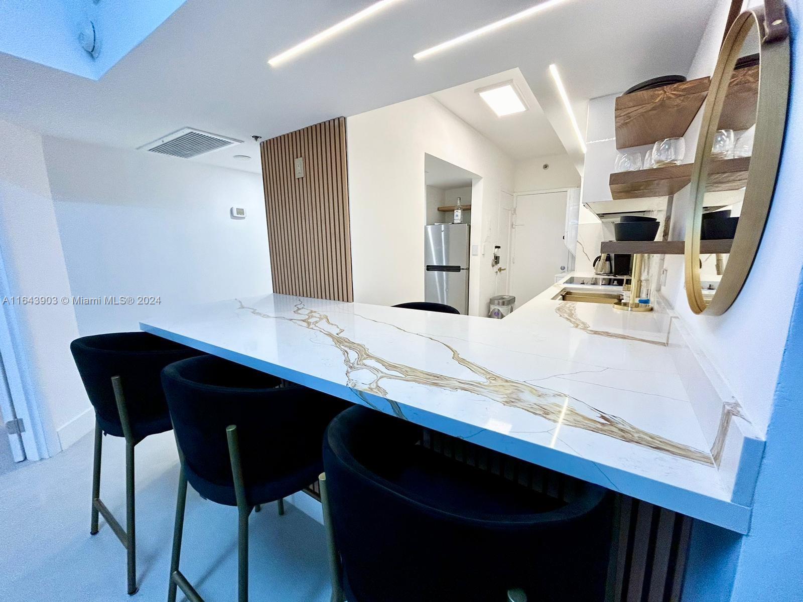 A kitchen features a white marble-veined breakfast bar, black stools, and wood-slat wall accents — 100 Lincoln Rd # 445, Miami Beach FL 33139, MIAMI BEACH, FL