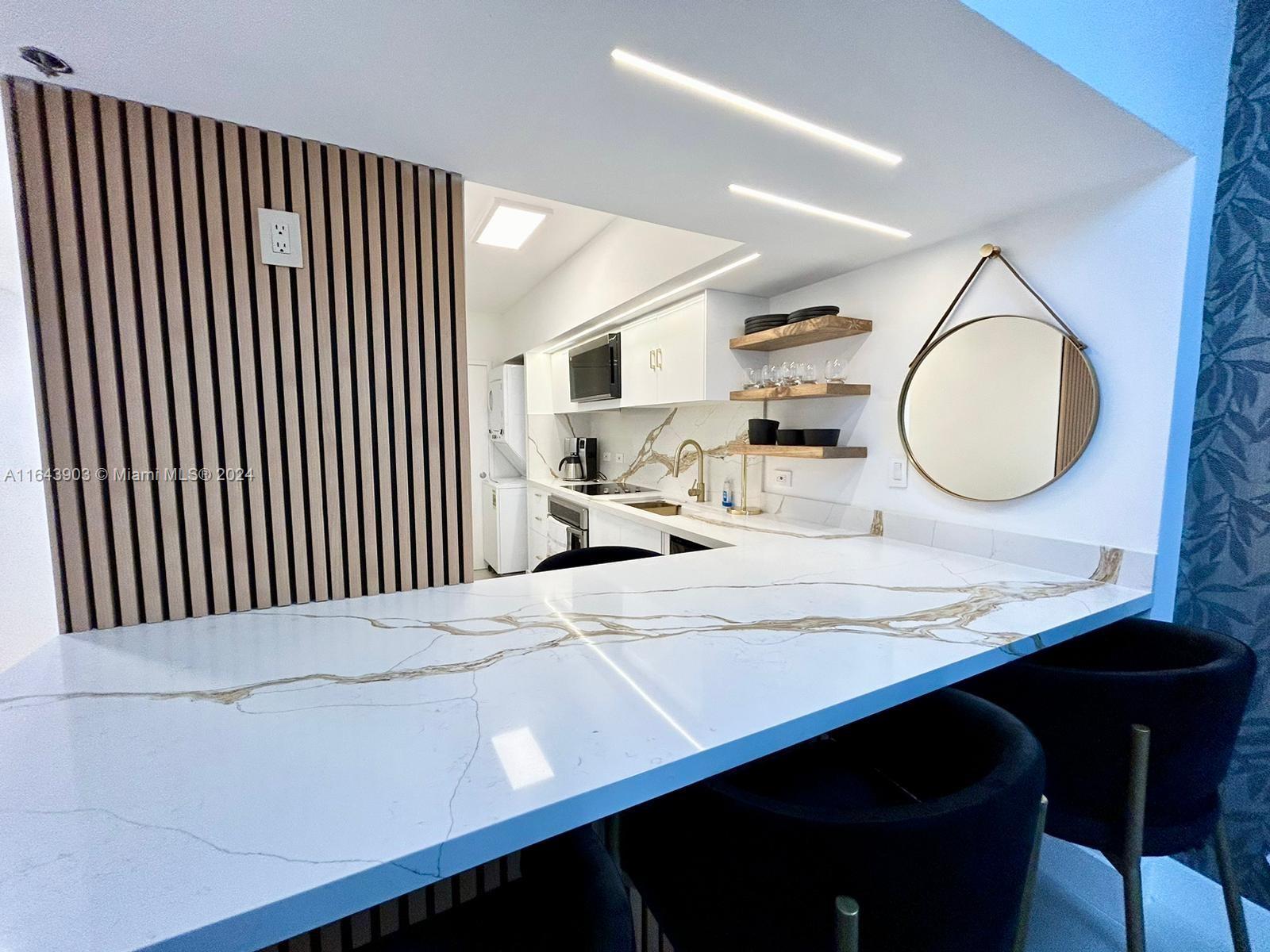 A modern kitchen features a marble-topped breakfast bar, wood slat wall, and floating shelves — 100 Lincoln Rd # 445, Miami Beach FL 33139, MIAMI BEACH, FL