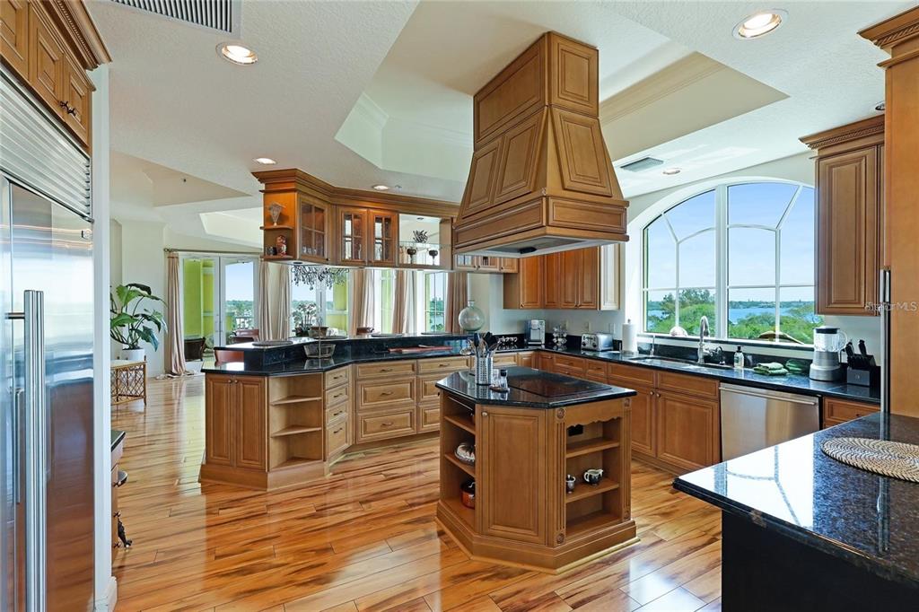 A spacious kitchen features wood cabinetry, dark granite countertops, a central island, and large windows — 1308 OLD STICKNEY POINT ROAD UNIT WP3, SARASOTA, FL