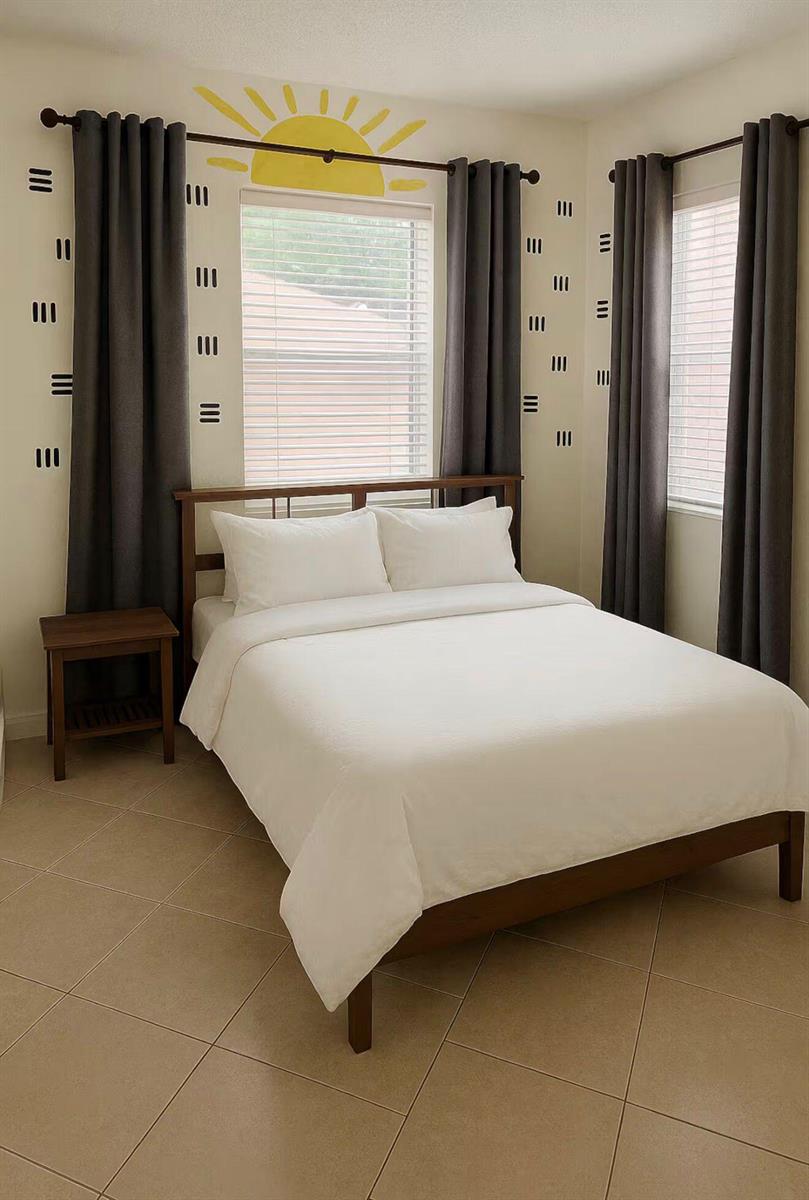 A bedroom with a queen bed, dark curtains, tile flooring, and a painted sun mural — 272 NE 44th Street, Deerfield Beach FL 33064, DEERFIELD BEACH, FL