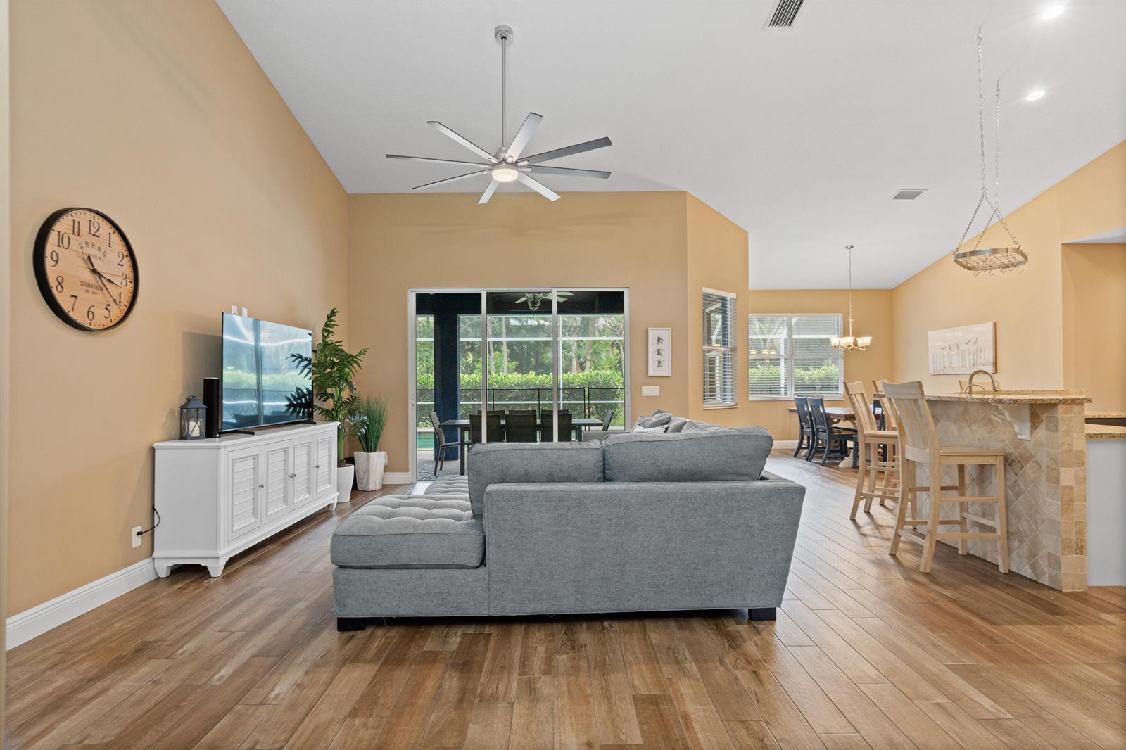 A living room with a gray sectional sofa, television console, and an open kitchen area — 11354 Sandy Run, FL 33478, FL