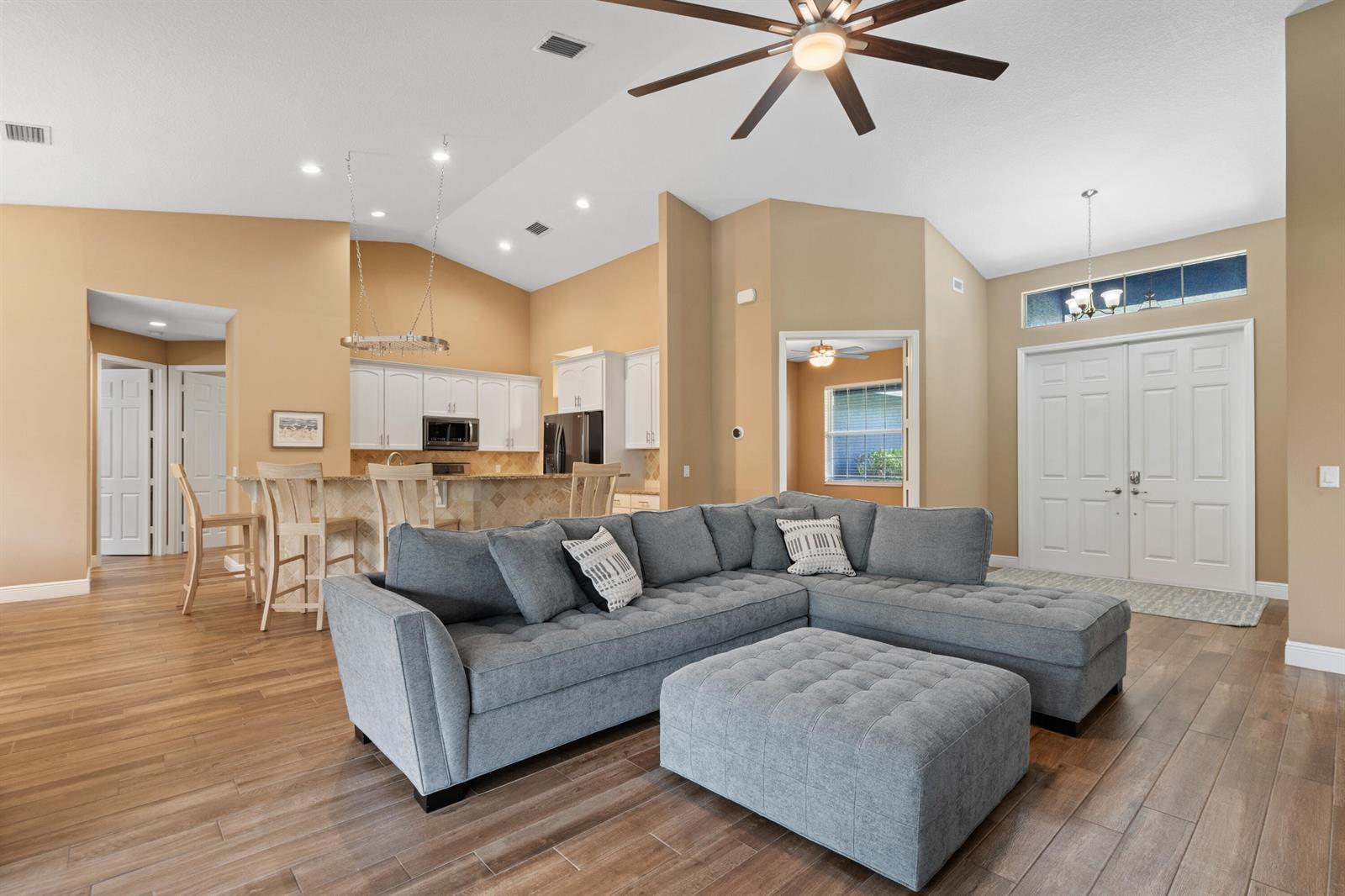 A living room with a gray sectional sofa, wood-look tile floors, and an open kitchen — 11354 Sandy Run, FL 33478, FL