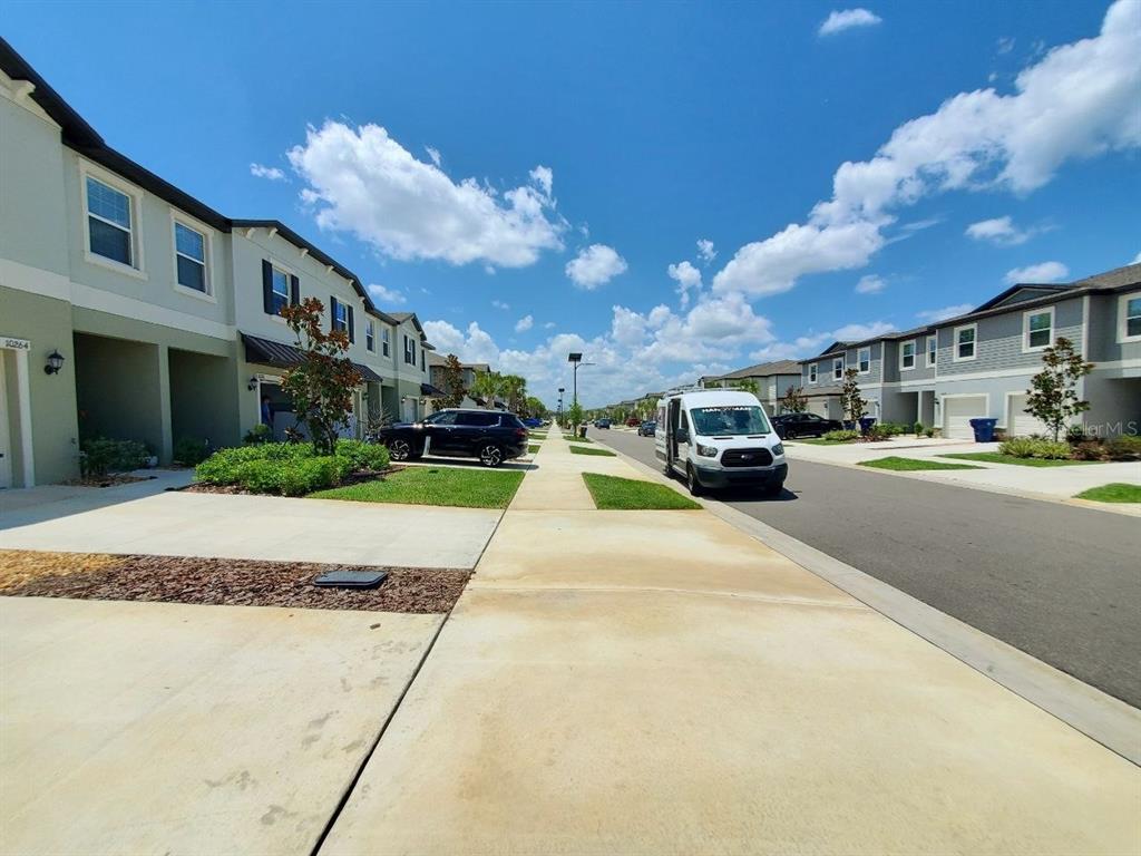 A street view of a residential neighborhood with townhomes, parked vehicles, and a sidewalk — 10268 TRUMPET HONEYSUCKLE WAY, SAN ANTONIO, FL