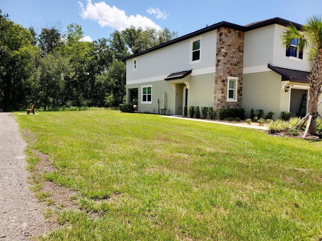 A two-story building with light-colored stucco walls, stone accents, and a grassy yard — 10268 TRUMPET HONEYSUCKLE WAY, SAN ANTONIO, FL
