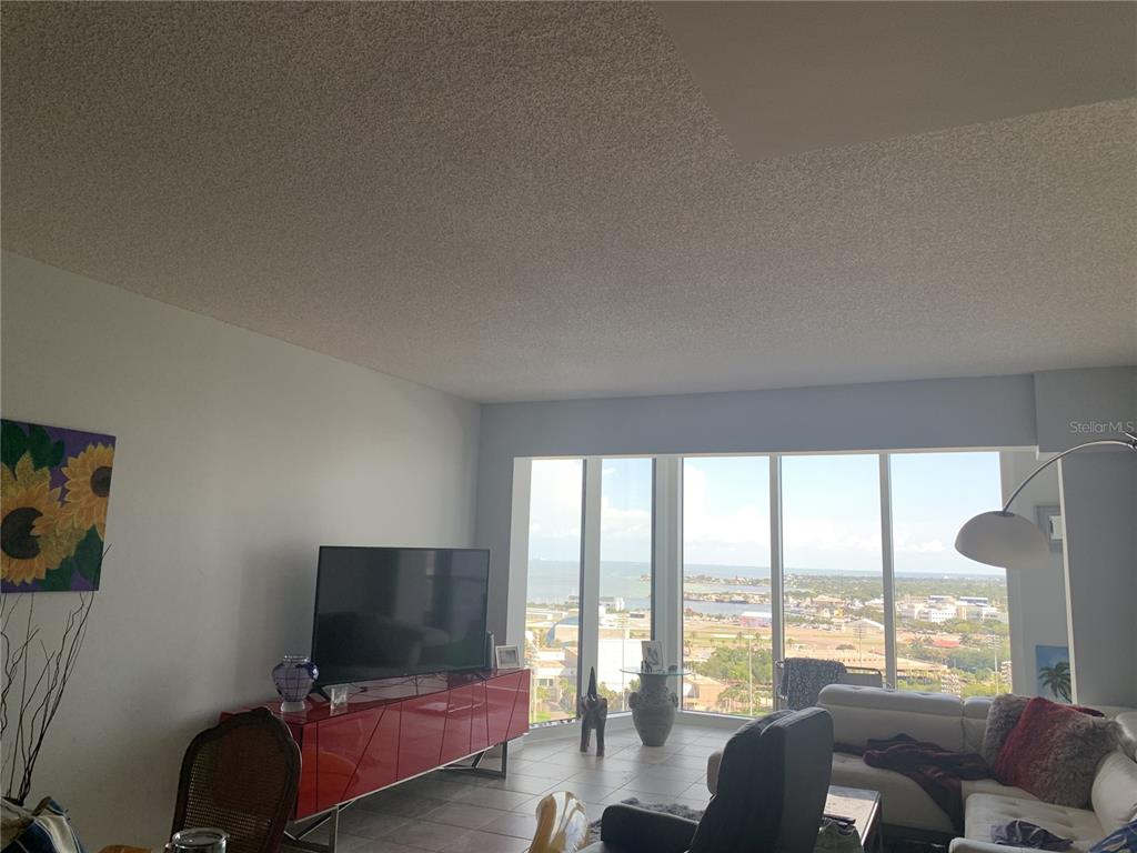 A living room features a red media console, a television, and floor-to-ceiling windows overlooking water — 1 BEACH DRIVE SE UNIT 1907, ST PETERSBURG, FL