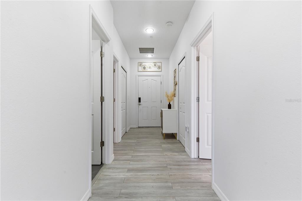 A bright hallway features light wood-look flooring, white walls, and several closed interior doors — 642 WELLS COURT UNIT 402, CLEARWATER, FL