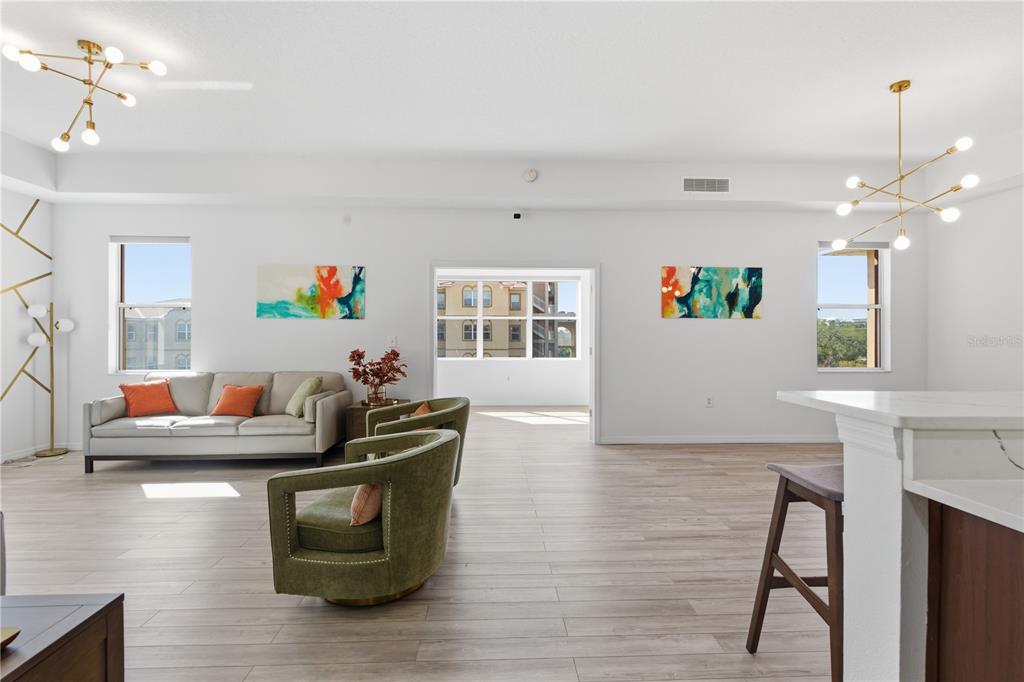 A bright, open-concept living area features light wood flooring, modern chandeliers, and two green armchairs — 642 WELLS COURT UNIT 402, CLEARWATER, FL