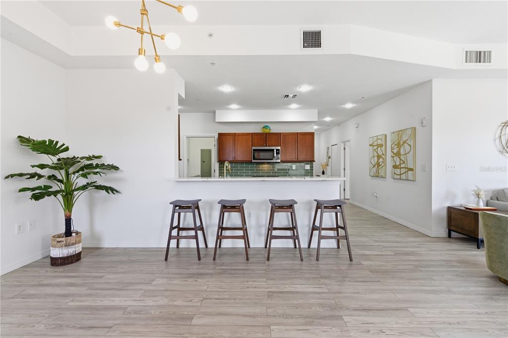 A kitchen with wood cabinets and a breakfast bar with four stools faces a living area — 642 WELLS COURT UNIT 402, CLEARWATER, FL
