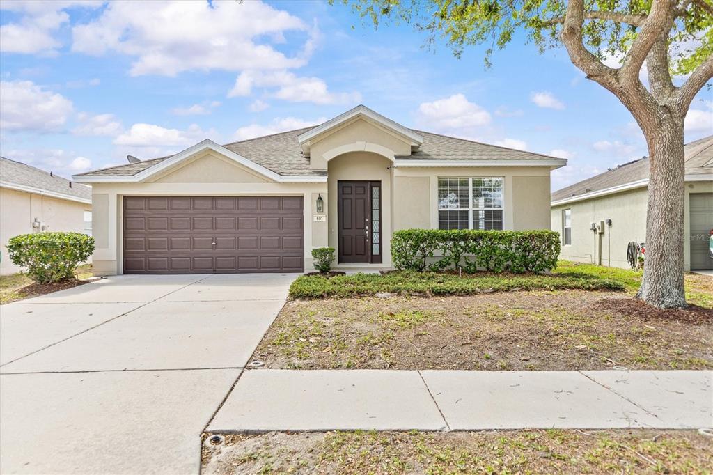 A single-story house with a beige stucco exterior, brown garage door, and a front lawn — 601 NODDING SHADE DRIVE, BROOKSVILLE, FL