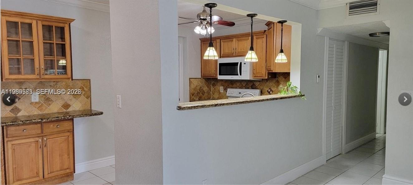 A kitchen with wood cabinets, granite countertops, and pendant lighting viewed from an adjacent room — 10835 SW 41st Ter, Miami FL 33165, MIAMI, FL