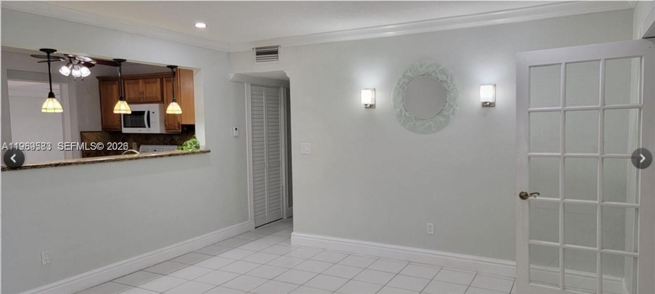 A dining area with white tile floors, wall sconces, a mirror, and a kitchen pass-through — 10835 SW 41st Ter, Miami FL 33165, MIAMI, FL