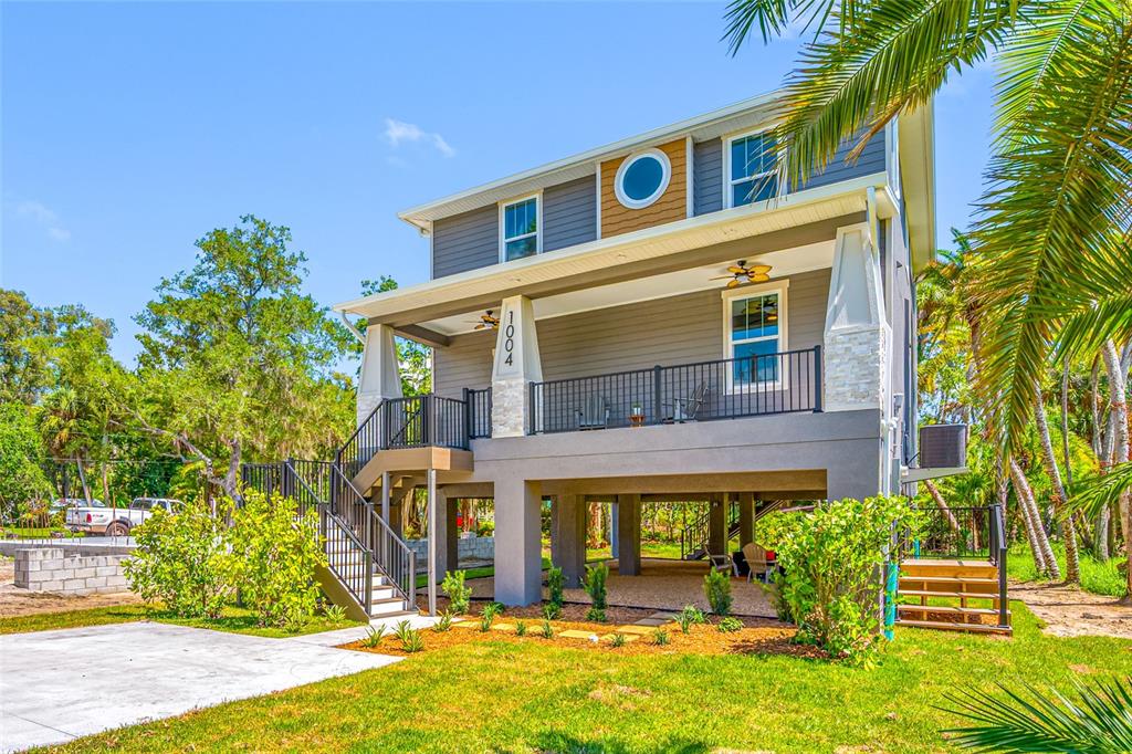 A two-story elevated house with a front porch, gray siding, and a concrete driveway — 1004 W HENRY AVENUE, TAMPA, FL