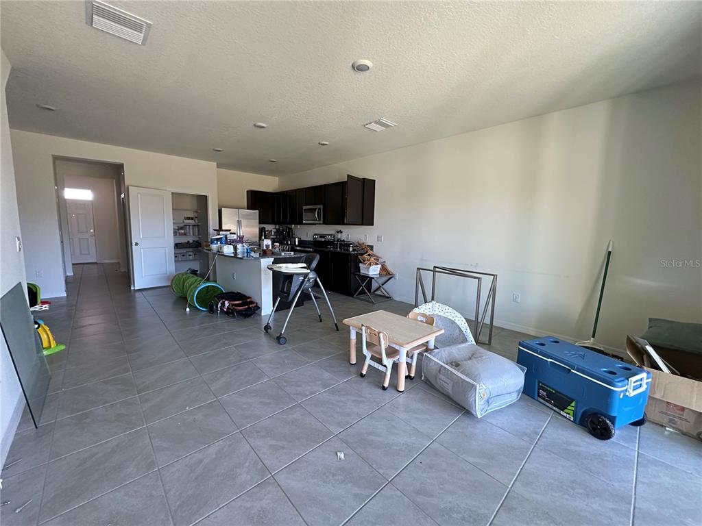 An open-concept kitchen and living area features dark cabinetry, tile flooring, and scattered furniture — 16641 GROTTO STEAM PLACE, WIMAUMA, FL
