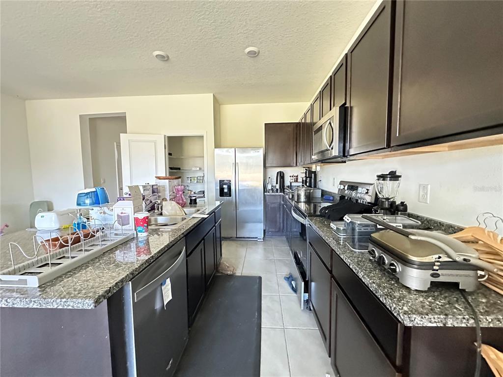 A kitchen features dark wood cabinets, granite countertops, stainless steel appliances, and a central island — 16641 GROTTO STEAM PLACE, WIMAUMA, FL