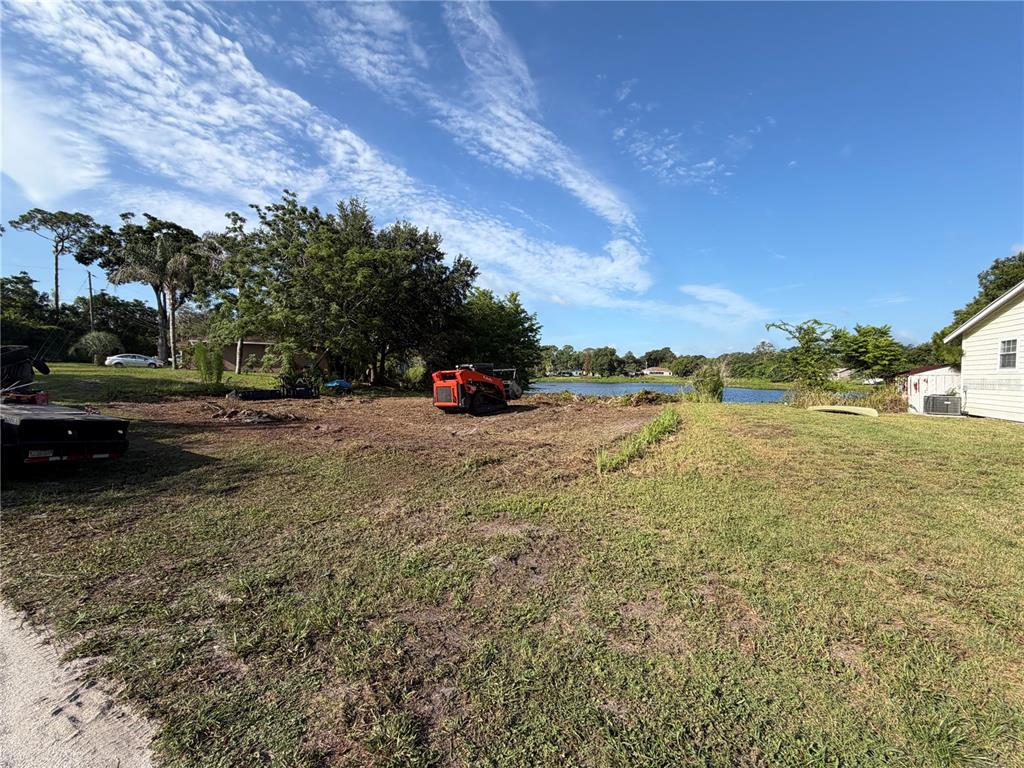 A cleared lot with a skid steer loader sits near a lake under a blue sky — 257 LAKE LANE, DEBARY, FL