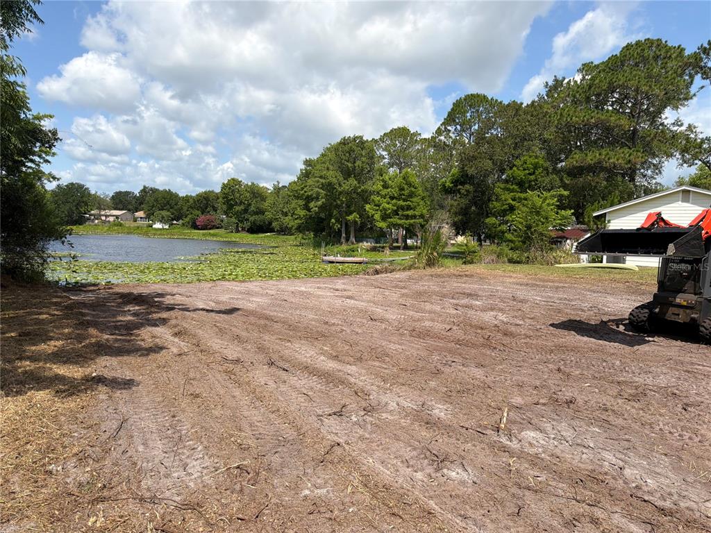 A cleared dirt lot sits adjacent to a lake with lily pads and surrounding trees — 257 LAKE LANE, DEBARY, FL