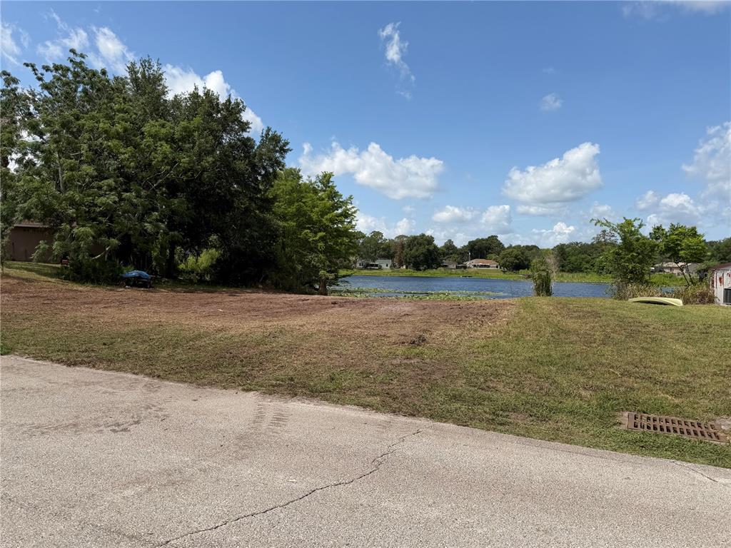 A vacant, grassy lot slopes down toward a small lake under a blue sky — 257 LAKE LANE, DEBARY, FL
