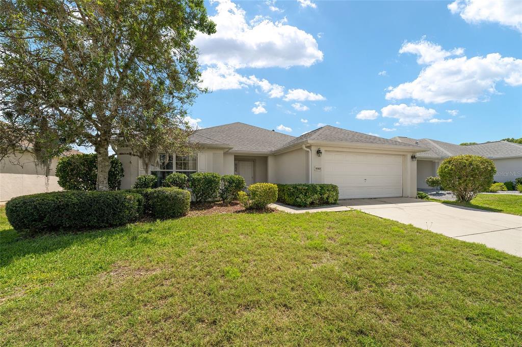 A single-story suburban house with a beige exterior, a two-car garage, and a front lawn — 8582 SE 133RD LANE, SUMMERFIELD, FL