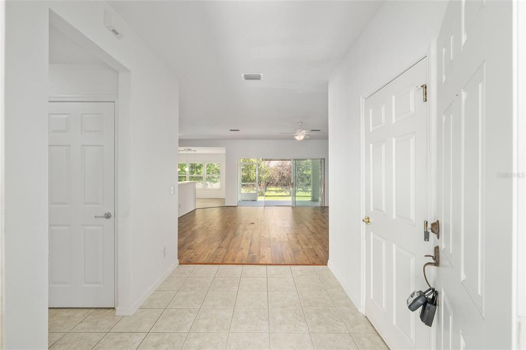 A tiled entryway leads into a living area with wood-look flooring and sliding glass doors — 8582 SE 133RD LANE, SUMMERFIELD, FL