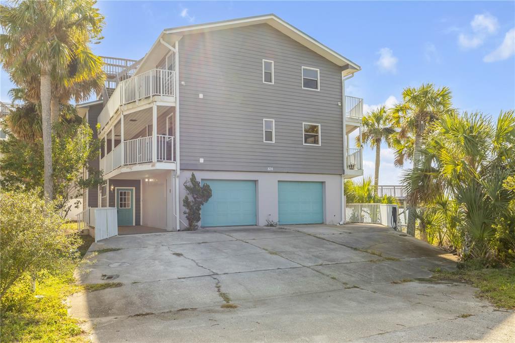 A three-story house with gray siding, two light blue garage doors, and a concrete driveway — 824 EEL AVENUE, NEW SMYRNA BEACH, FL