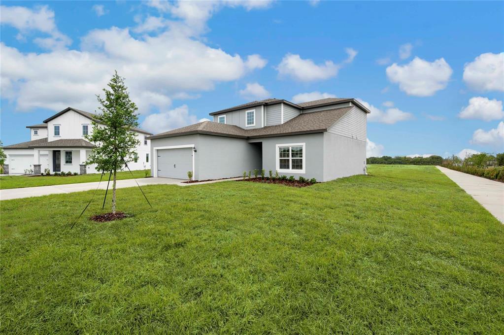 A two-story gray house with a garage and a large grassy yard under a blue sky — 624 TANGELO TERRACE, BABSON PARK, FL