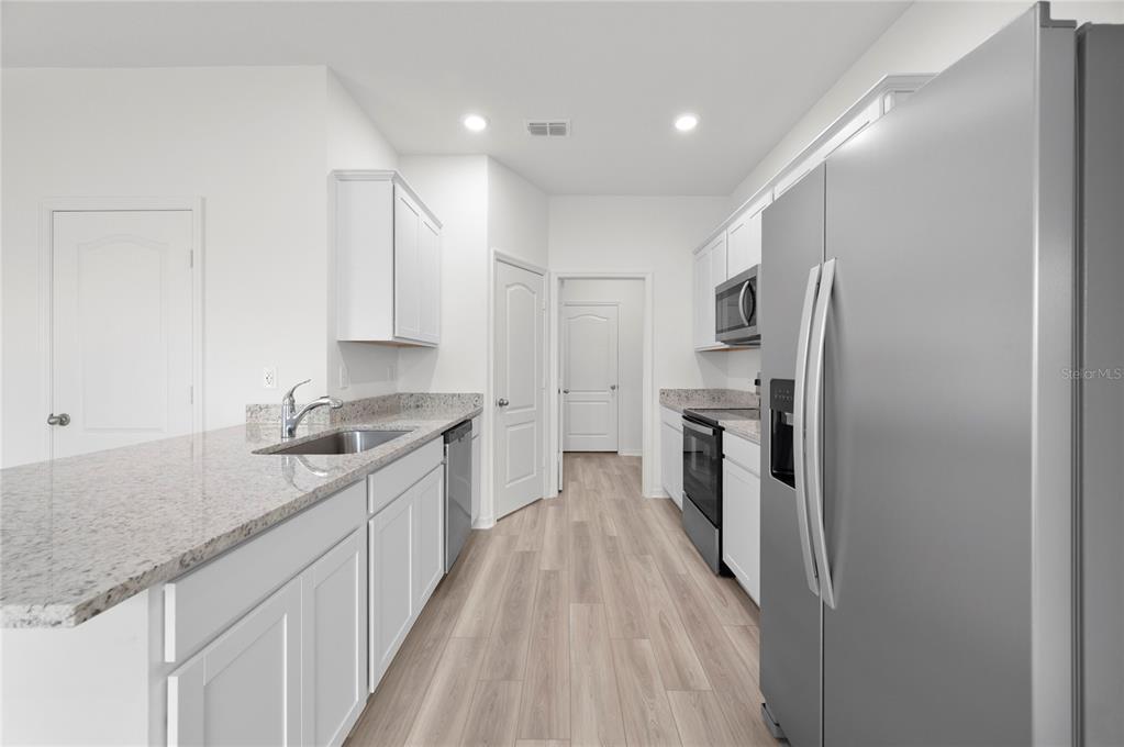 A modern kitchen features white cabinets, granite countertops, stainless steel appliances, and light wood flooring — 624 TANGELO TERRACE, BABSON PARK, FL