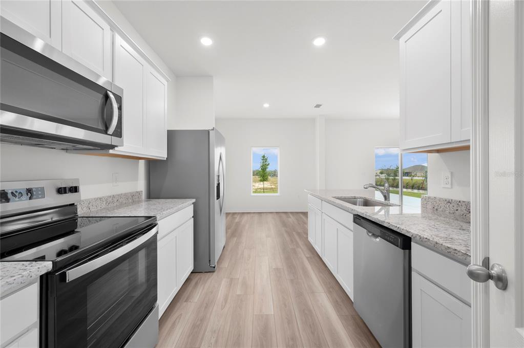 A modern kitchen features white cabinets, granite countertops, stainless steel appliances, and light wood flooring — 624 TANGELO TERRACE, BABSON PARK, FL