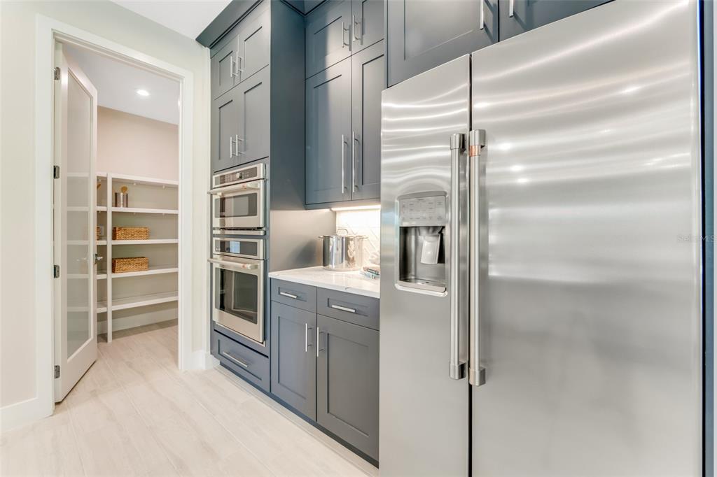 A kitchen features dark blue cabinetry, stainless steel appliances, and an adjacent walk-in pantry — 1214 CRESSWIND BOULEVARD, DELAND, FL